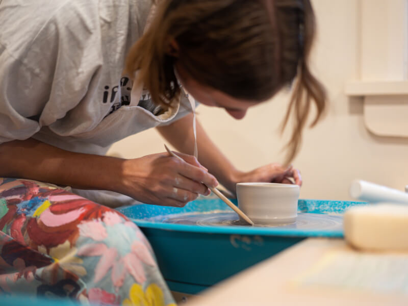 A close up of a person taking a handmade clay pot off of a pottery wheel